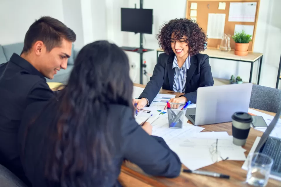 Couple on one side of desk with banker on other side looking at paperwork.